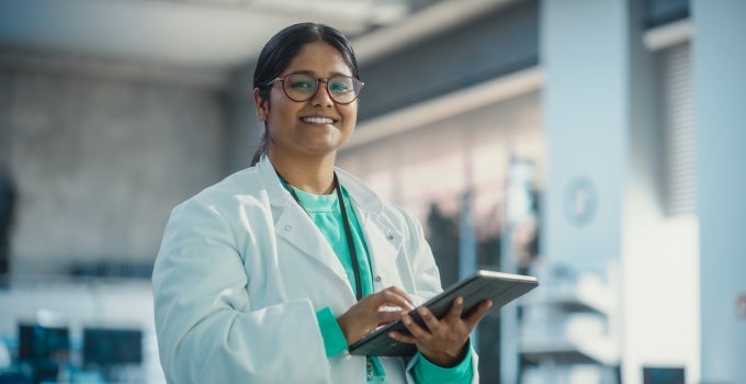 Indian female graduate student in lab coat with tablet