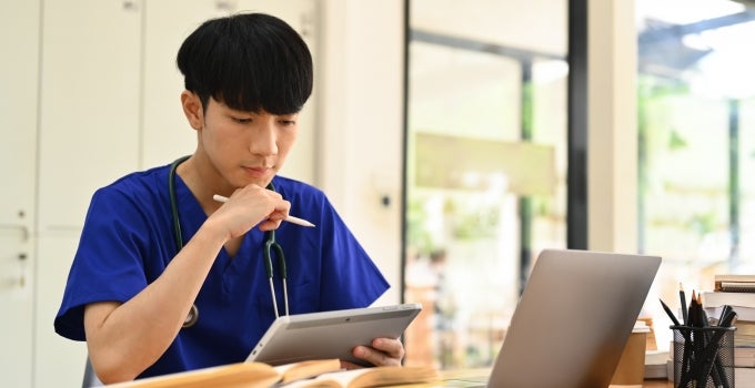 Asian male nurse in blue scrubs studying